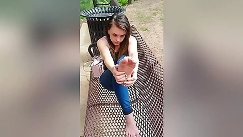 Beautiful teen 18+ In Jeans Sitting On The Bench Outdoors Playing With Her Feet
